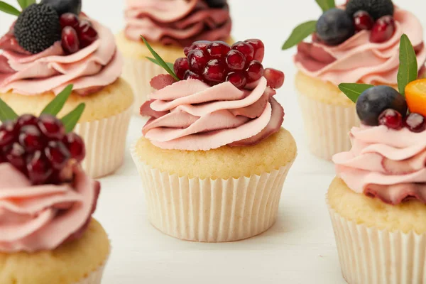 Foco seletivo de cupcakes com creme e bagas na superfície branca — Fotografia de Stock