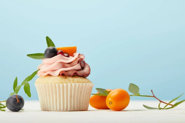 Tasty cupcake with cream and kumquats on white surface isolated on blue — Stock Photo