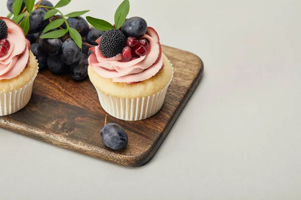 Planche à découper en bois avec cupcakes sucrés isolés sur gris — Photo de stock