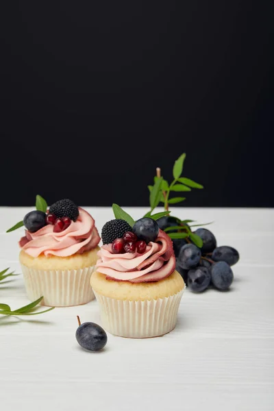 Cupcakes with cream and berries on white surface isolated on black — Stock Photo