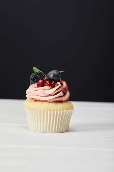 Cupcake with berries on white surface isolated on black — Stock Photo