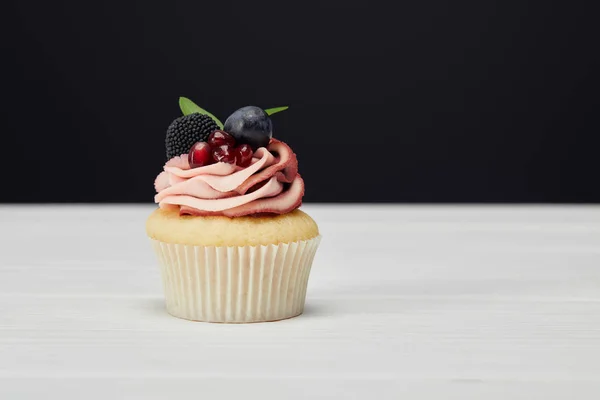 Cupcake with berries on white surface isolated on black — Stock Photo