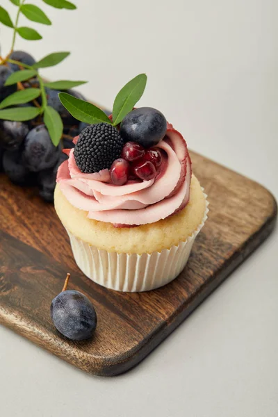 Cupcake à la crème et raisins sur planche à découper isolé sur gris — Photo de stock