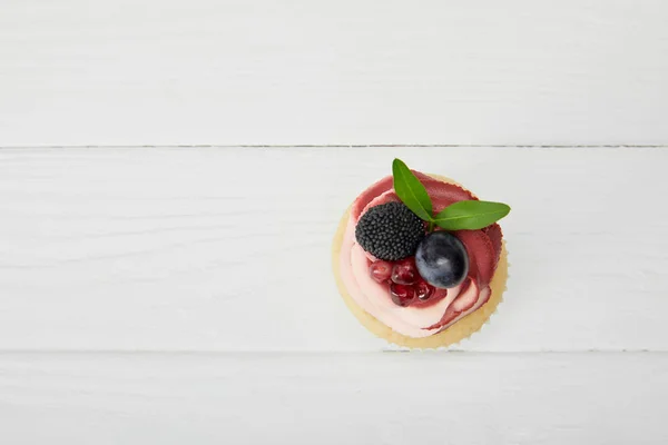 Top view of cupcake with grape, garnet and blackberry on white wooden surface — Stock Photo