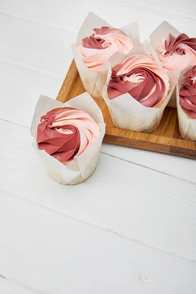 Cupcakes with cream on cutting board on white surface — Stock Photo