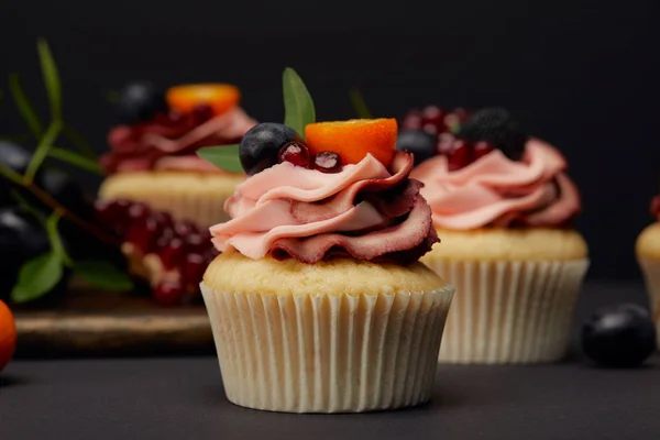 Cupcakes with fruits and berries on grey surface isolated on black — Stock Photo