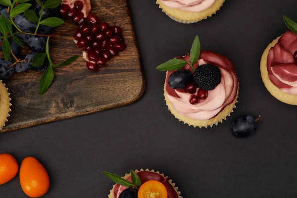 Top view of cupcakes, grapes, garnet and cutting board on black surface — Stock Photo