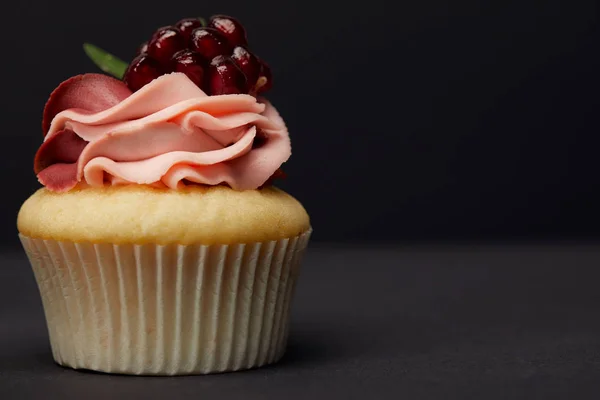 Cupcake with garnet on grey surface isolated on black — Stock Photo