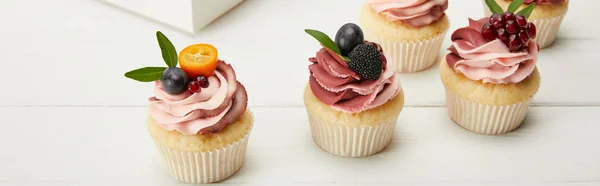 Panoramic shot of cupcakes with fruits and berries on white surface — Stock Photo