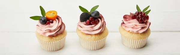 Panoramic shot of cupcakes with fruits and berries on white surface — Stock Photo