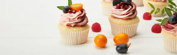 Panoramic shot of cupcakes with fruits and berries on white surface — Stock Photo