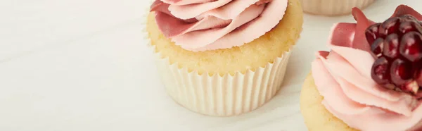 Panoramic shot of cupcakes with cream and garnet on white surface — Stock Photo