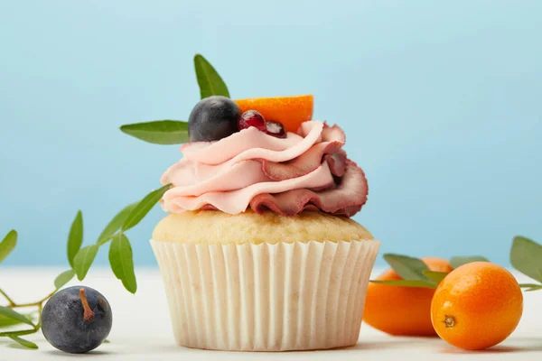 Cupcake con crema, uva e kumquat su superficie bianca isolata su blu — Foto stock