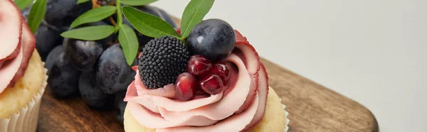 Panoramic shot of cupcakes with cream and berries on cutting board isolated on grey — Stock Photo