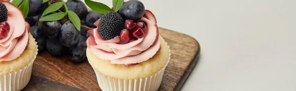 Panoramic shot of cupcakes with cream and berries on cutting board isolated on grey — Stock Photo