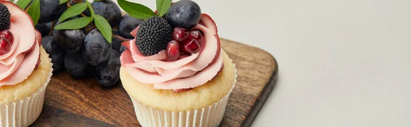 Panoramaaufnahme von Cupcakes mit Sahne und Beeren auf Schneidebrett isoliert auf grau — Stockfoto