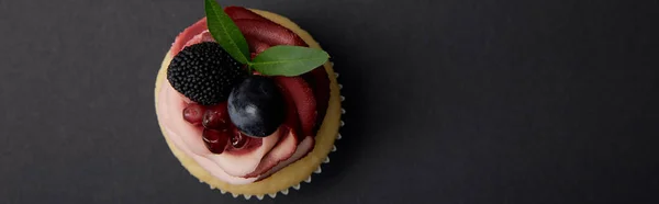 Panoramic shot of cupcake with cream, garnet, grape and blackberry on black surface — Stock Photo