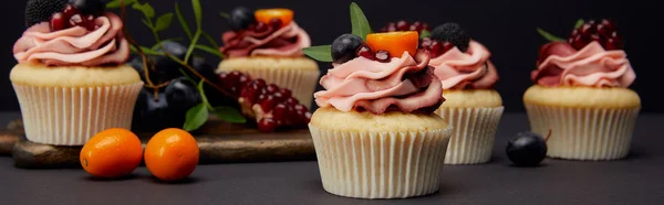 Panoramic shot of cupcakes with cream, fruits and berries isolated on black — Stock Photo