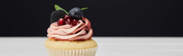 Panoramaaufnahme von Cupcake mit Sahne, Granat und Beeren auf weißer Oberfläche isoliert auf schwarzer — Stockfoto