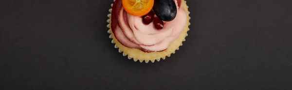 Panoramic shot of cupcake with cream and fruits on black surface — Stock Photo