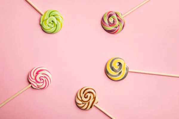 Vista superior de deliciosas piruletas de remolino multicolores sobre palos de madera sobre fondo rosa - foto de stock