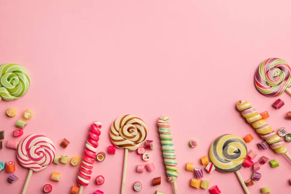 Draufsicht auf köstliche bunte Wirbellutscher auf Holzstäben und Bonbons auf rosa Hintergrund — Stockfoto