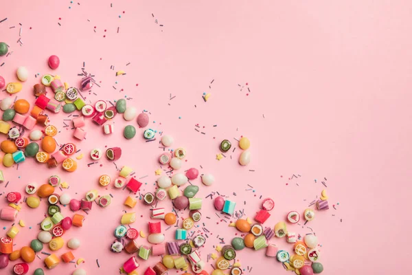 Top view of colorful candies and sprinkles scattered on pink background with copy space — Stock Photo