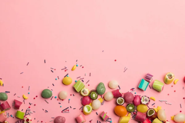 Vue de dessus de bonbons sucrés colorés et saupoudrer éparpillés sur fond rose avec espace de copie — Photo de stock