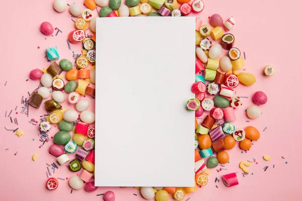 Top view of delicious multicolored candies and white blank card with copy space on pink background — Stock Photo