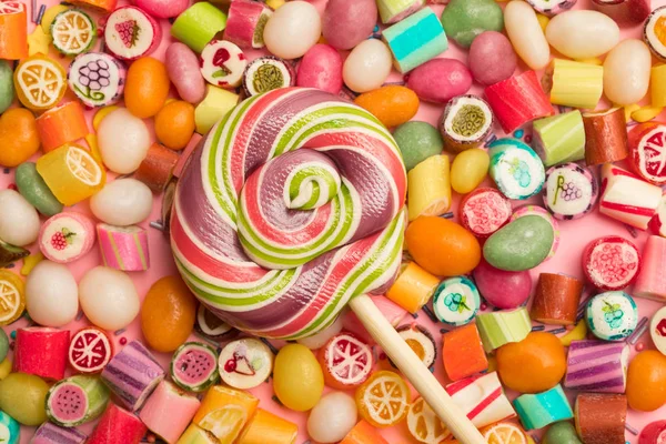 Вид сверху на яркие вкусные разноцветные карамельные конфеты и круговой леденец на деревянной палочке — стоковое фото
