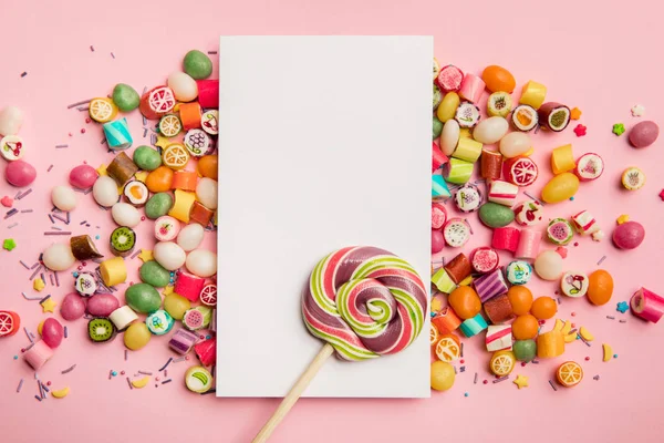 Vista superior de doces deliciosos, pirulito e cartão branco com espaço de cópia no fundo rosa — Fotografia de Stock