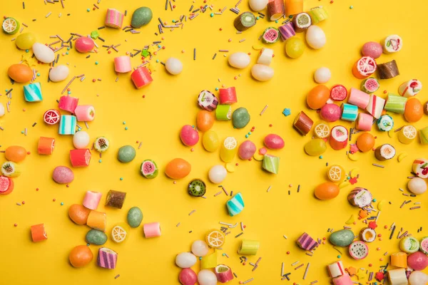Вид сверху на разноцветные конфеты и брызги, разбросанные на желтом фоне — стоковое фото
