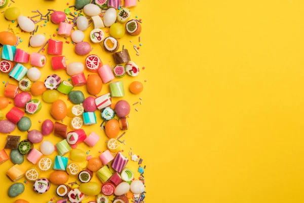 Вид сверху разноцветных конфет и брызг, разбросанных на желтом фоне с копировальным пространством — стоковое фото