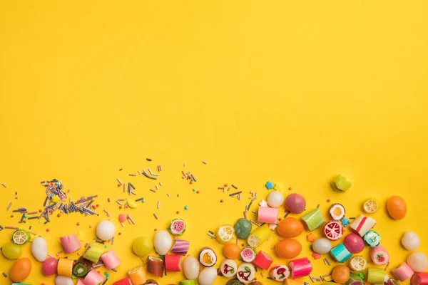 Vista superior de doces saborosos multicoloridos e polvilhas espalhadas no fundo amarelo com espaço de cópia — Fotografia de Stock