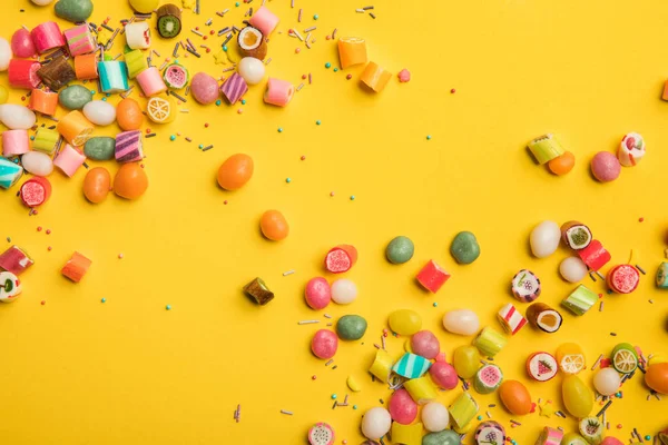 Vista superior de dulces sabrosos multicolores dispersos sobre fondo amarillo con espacio para copiar - foto de stock