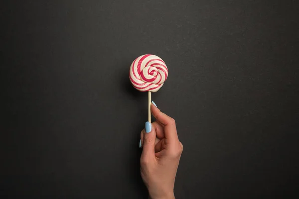 Cropped view of woman holding round tasty lollipop on black background — Stock Photo