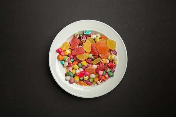 Vista dall'alto di deliziose caramelle multicolori al caramello e gelatine di agrumi in piatto bianco su sfondo nero — Foto stock