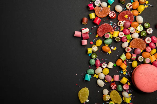 Вид сверху на вкусные разноцветные конфеты, брызги и макароны на черном фоне — стоковое фото