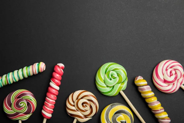 Top view of delicious multicolored round and swirl lollipops on wooden sticks on black background — Stock Photo