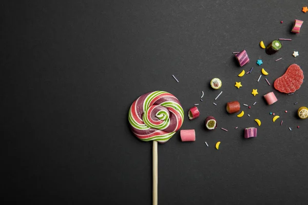 Vista dall'alto di deliziosi lecca-lecca rotondi multicolore su bastone di legno con caramelle e spruzzi su sfondo nero — Foto stock