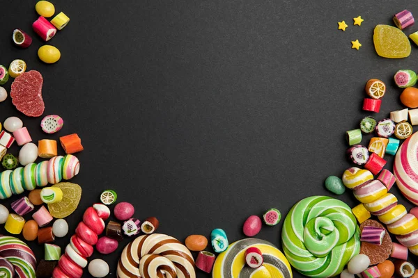 Top view of delicious multicolored swirl and round lollipops, candies, jellies and sprinkles on black background — Stock Photo