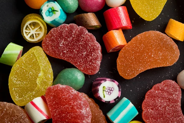 Vista de cerca de caramelos multicolores de caramelo y jaleas de frutas azucaradas sobre fondo negro - foto de stock