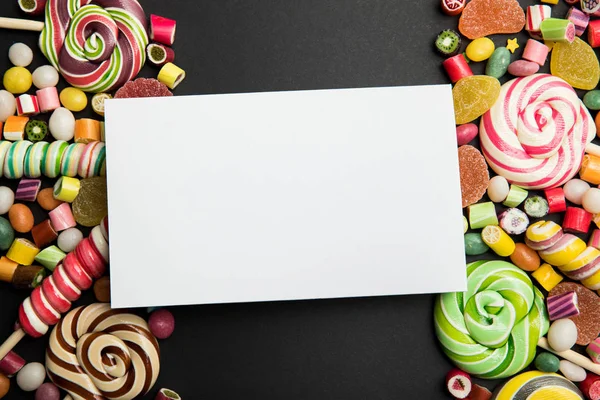 Draufsicht auf köstliche bunte Süßigkeiten und leere weiße Karte auf schwarzem Hintergrund — Stockfoto