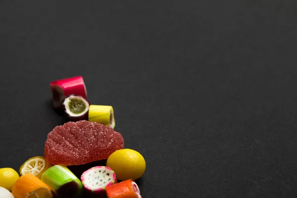 Deliciosos dulces de caramelo de frutas multicolores sobre fondo negro con espacio para copiar - foto de stock