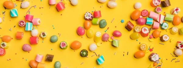 Plano panorámico de caramelos multicolores y salpicaduras esparcidas sobre fondo amarillo - foto de stock