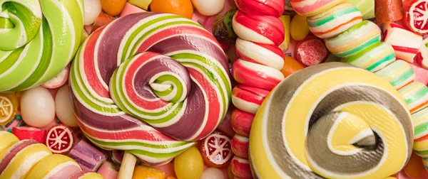 Panoramic shot of bright round and swirl lollipops on fruit caramel candies — Stock Photo