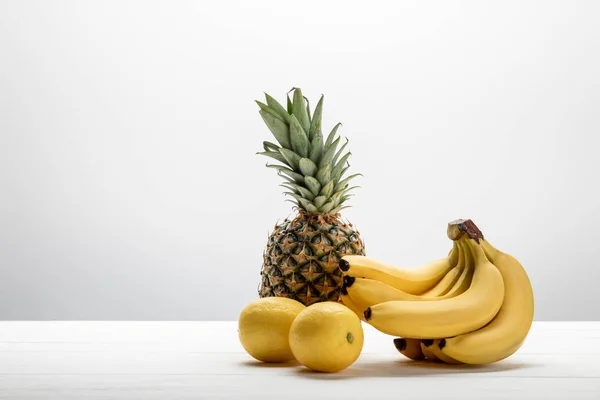 Reife gelbe Bananen in der Nähe von süßer Ananas und Zitronen auf weiß — Stockfoto