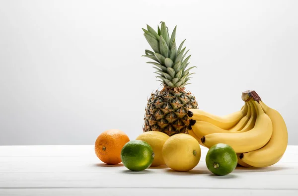 Bananas maduras perto de abacaxi doce, limões, laranja e limas em branco — Fotografia de Stock