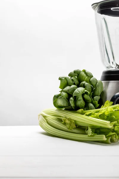 Grüne frische Spinatblätter in der Nähe von Bio-Sellerie und Mixer auf weißem — Stockfoto