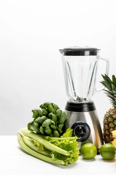 Green fresh spinach leaves near organic celery, lime,pineapple and blender on white — Stock Photo